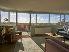 A living room with a sofa and chair near large windows at Harbour Lights in Southwold