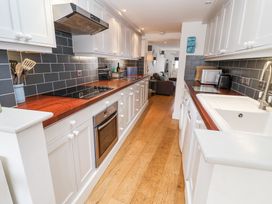 A galley kitchen with white cabinets wooden countertops and black tiled backsplash at Dolphin Cottage Southwold