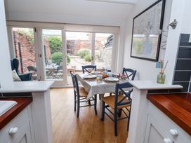A kitchen dining area with a table set for breakfast and four blue chairs near glass doors leading to a garden at Dolphin Cottage Southwold