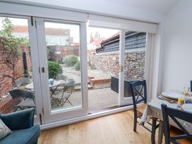 A dining area with a table set for breakfast and blue chairs next to glass sliding doors opening to a small outdoor patio with a round table and four chairs at Dolphin Cottage Southwold