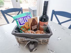 A basket with a bottle of Malbec wine a chocolate bar pretzels and cookies on a table with seagull patterned tablecloth at Dolphin Cottage Southwold
