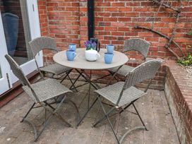 An outdoor patio area with a round table, four chairs, a white teapot, a black French press, four blue mugs, and a small purple flower arrangement at Dolphin Cottage Southwold