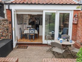 An outdoor patio area with a round table and four chairs and an open view into a dining area with a table and four chairs at Dolphin Cottage Southwold