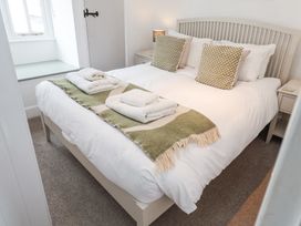 A bedroom with a bed with white linens and green patterned pillows and folded towels on a green runner at Dolphin Cottage Southwold
