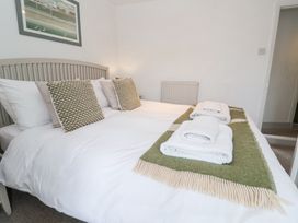 A bedroom with a bed made with white linens and patterned pillows a green and beige throw and folded towels on the bed at Dolphin Cottage Southwold