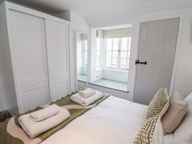 A bedroom with a bed with folded towels on it a window seat a white wardrobe and a closed door at Dolphin Cottage Southwold