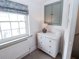 A corner of a room with a white chest of drawers lamp and small cabinet under a closed wall cupboard at Dolphin Cottage Southwold