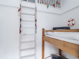 A wooden bunk bed with folded blankets and a white ladder decorated with small fish ornaments in a white room at Dolphin Cottage Southwold