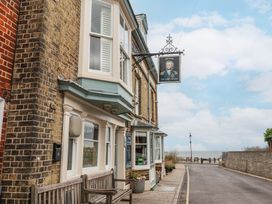 A street view of a brick building with a bench outside and a sign showing a portrait with the sea visible at the end of the road at Dolphin Cottage Southwold