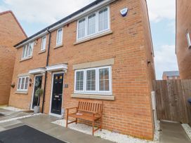 A front view of a brick house with black doors white framed windows and a wooden bench outside at Happy Days in Bridlington