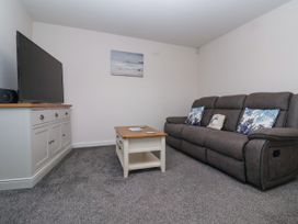 A living room with a gray sofa and three pillows a white coffee table and a white TV cabinet with a television on top at Happy Days in Bridlington