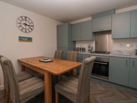 A kitchen with a wooden dining table and striped chairs a clock on the wall and blue cabinets with a stove at Happy Days in Bridlington