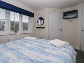 A bedroom with a bed covered in a blue and white patterned duvet two folded towels a window with blinds and dark blue valance a round mirror on the wall and a wall mounted TV at Happy Days in Bridlington