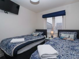 A bedroom with two single beds with blue patterned bedding a window between them with blinds and a blue valance a bedside table with a lamp and a decorative sailboat and a wall-mounted television at Happy Days in Bridlington