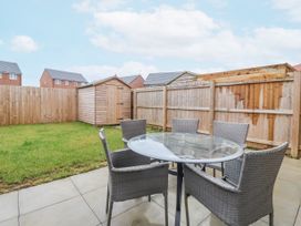 A backyard with a glass table and six wicker chairs on a patio next to a grass lawn and a wooden shed at Happy Days in Bridlington