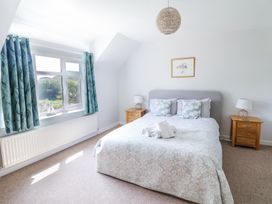 A bedroom with a bed between two wooden bedside tables by a window with blue curtains at The Seaside Inn in Beer