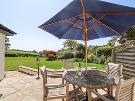 An outdoor patio with a round wooden table under a blue umbrella and four wooden chairs overlooking a garden at The Seaside Inn in Beer