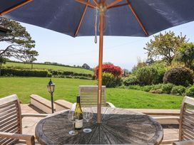 A garden patio with wooden table and chairs under a blue umbrella overlooking a lawn and shrubs at The Seaside Inn in Beer