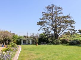 A garden with a lawn a small building a large tree and flower beds at The Seaside Inn in Beer