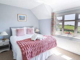 A bedroom with a bed pink pillows and blanket bedside tables and a window with a view at The Beach House in Beer