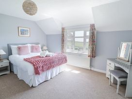 A bedroom with a bed with pink pillows and blanket next to a window and a dressing table with a mirror at The Beach House in Beer