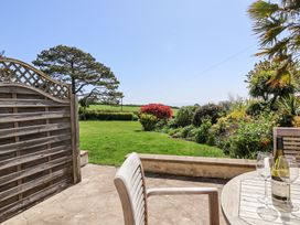 A patio with wooden chairs and a table with wine glasses and bottle overlooking a garden with bushes and lawn at The Beach House in Beer