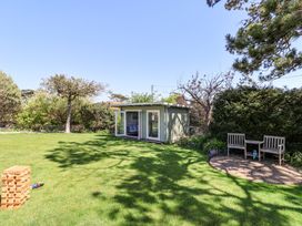 A garden with a small green shed a wooden bench set on a stone patio and a lawn with giant wooden blocks at The Beach House in Beer