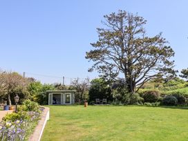A garden with a lawn a small building a large tree and outdoor chairs at The Beach House in Beer