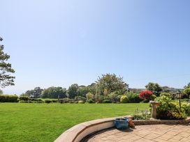 A garden with a green lawn and flowerbeds beside a paved patio at The Beach House in Beer