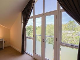 A room with large glass doors and windows with brown curtains and a white desk at Fig Tree House in Axminster