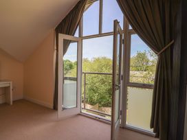 A room with beige walls and carpet with an open glass door leading to a balcony with trees outside at Fig Tree House Axminster