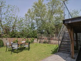 A garden area with a table and six chairs on grass and wooden stairs leading to a raised deck at Fig Tree House in Axminster