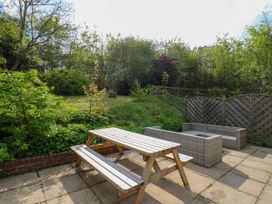 An outdoor patio with a wooden picnic table and wicker seating surrounded by trees and greenery at Waldegrave Barn Hartest near Glemsford