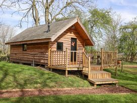 A wooden cabin with a small porch and stairs in a grassy area with trees at Duck Lodge in Bedale