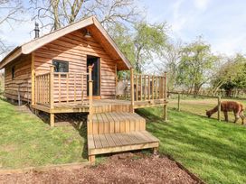 A cabin with a small wooden deck and steps surrounded by grass and trees with an animal grazing at Duck Lodge in Bedale