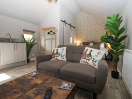 A living area with a gray sofa and duck print cushions a wooden coffee table with a remote control a wooden rack and bed in the background at Duck Lodge in Bedale