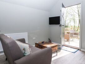 A small living room with a gray couch a wooden coffee table a wall-mounted television and an open door leading to an outdoor deck with wicker chairs at Duck Lodge in Bedale