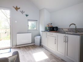 A kitchen area with white cabinets a sink a kettle toaster and a microwave beside a door and window at Duck Lodge in Bedale