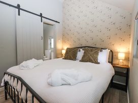 A bedroom with a bed white bedding two brown pillows two bedside tables with lamps and a sliding door leading to a bathroom at Duck Lodge in Bedale