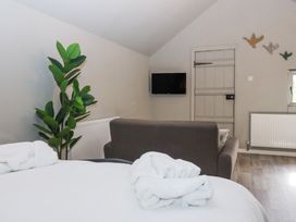 A room with a bed covered in white linens and towels a gray sofa a wall-mounted television a green plant and a wooden door at Duck Lodge in Bedale
