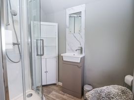 A bathroom with a glass shower enclosure a white cabinet a sink with a mirror and a grey ottoman at Duck Lodge in Bedale