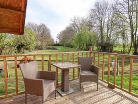 A wooden deck with two chairs and a small table overlooking a fenced grassy area with trees at Duck Lodge in Bedale