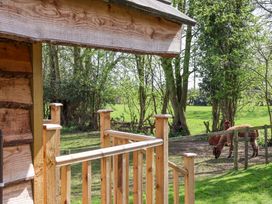 A wooden porch railing with trees and two brown alpacas in a fenced area at Duck Lodge in Bedale