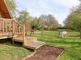 A wooden deck with steps leading to a fenced grassy area with two alpacas and trees in the background at Duck Lodge in Bedale