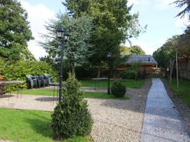 An outdoor garden area with gravel paths tables stacked chairs and a wooden shed at Duck Lodge in Bedale