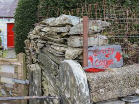 A stone wall with a metal gate and a sign reading Quarry Cottage in front of a white building with a red door at Quarry Cottage in Blaenau Ffestiniog
