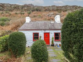 A stone cottage with red door and window frames surrounded by greenery and hills at Quarry Cottage in Blaenau Ffestiniog