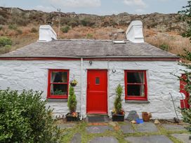 A stone cottage with red door and window frames with plants and rocky hill behind at Quarry Cottage in Blaenau Ffestiniog