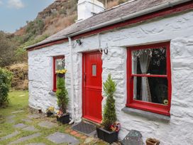 The exterior of a white stone cottage with a red door and red window frames and potted plants near the entrance at Quarry Cottage in Blaenau Ffestiniog