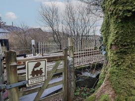 A wooden gate with a train crossing warning sign near railway tracks and a moss-covered tree at Quarry Cottage in Blaenau Ffestiniog